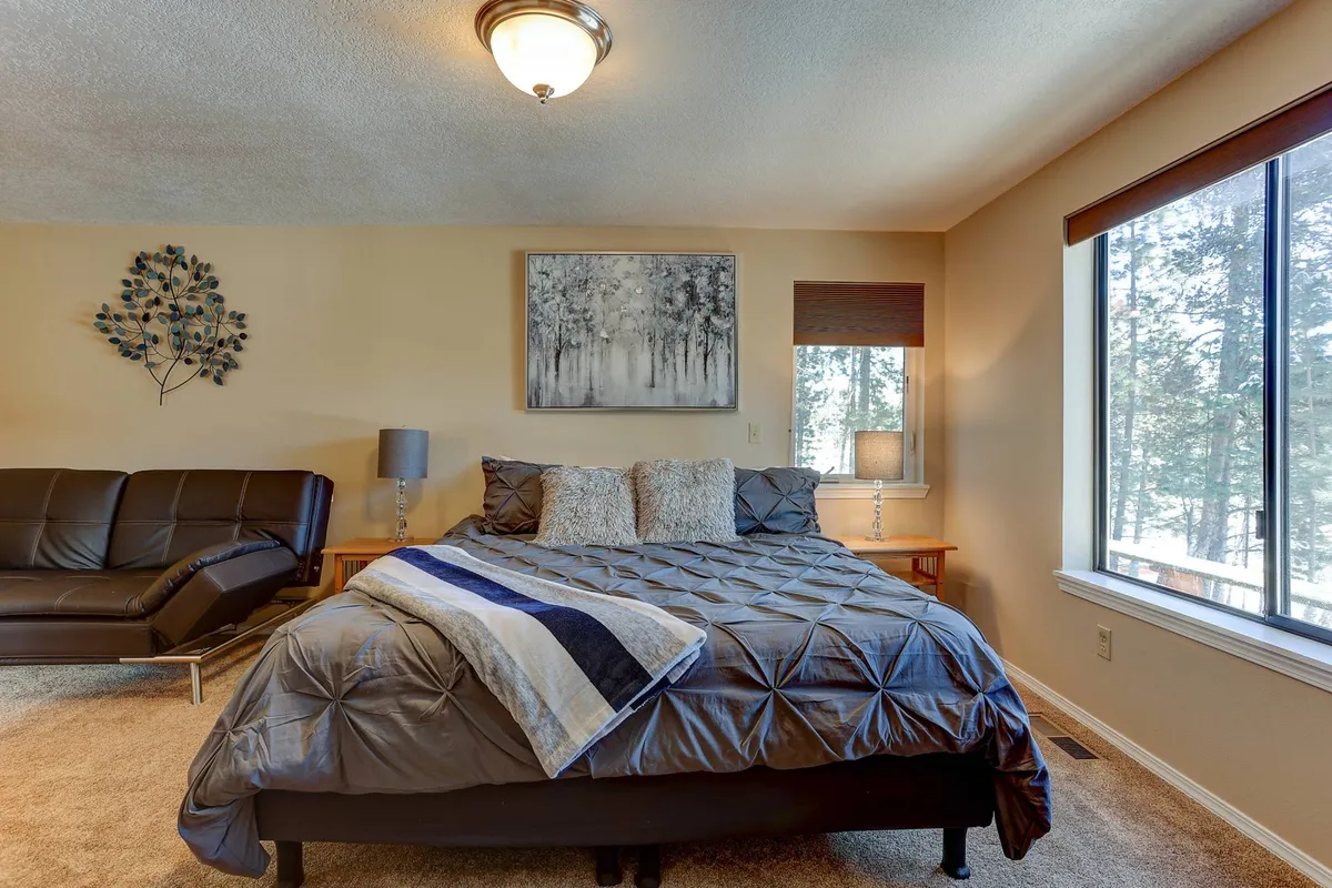 A cozy bedroom scene with a bed, a sofa placed near a window, and soft natural light filling the space. The setup suggests additional sleeping options and a peaceful retreat.
