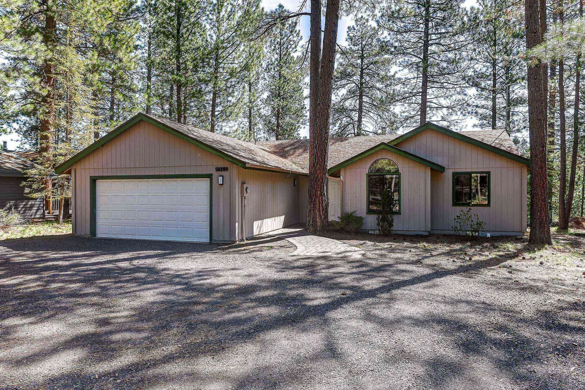 An inviting exterior shot showcasing the home's front entrance, spacious garage, and large windows framed by natural landscapes. The driveway and garage are clearly visible, hinting at secure parking and easy access for outdoor toys and vehicles.