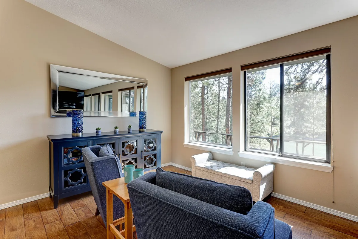 A cozy, serene interior lounge with comfortable seating, blue accent decor, a large mirror, and wooden furniture. Sunlight streams in through the window, creating a warm, inviting atmosphere ideal for relaxing or gathering with friends.
